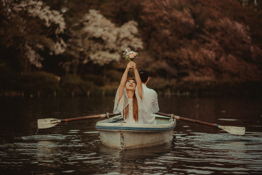 A couple rowing the boat on the lake with a cherry tree in the background