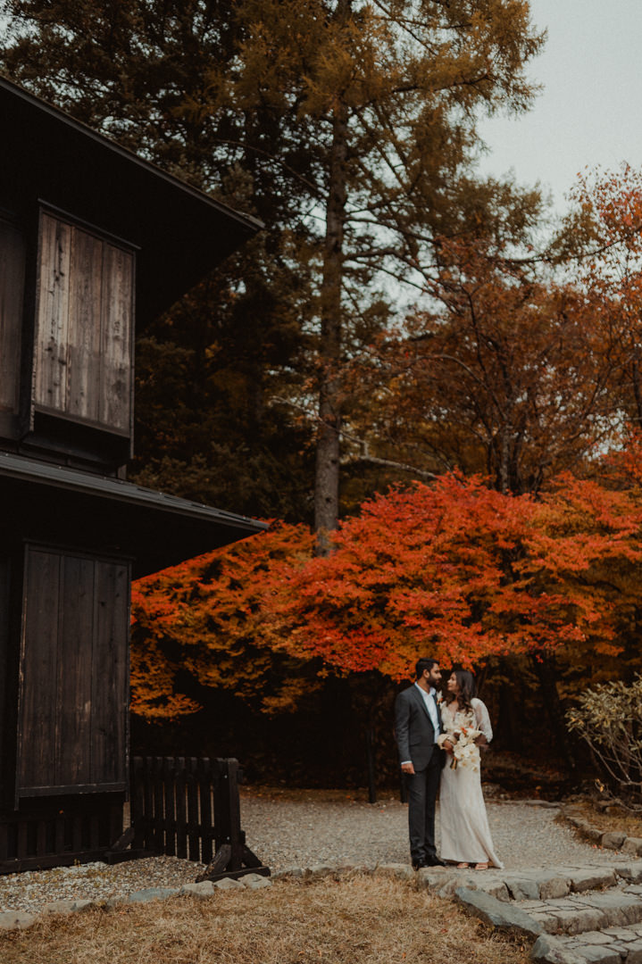Couple standing under orange tree on their fall elopement in Japan