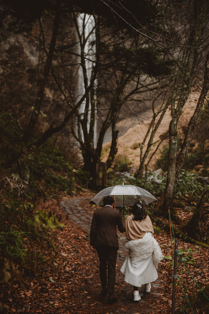Japan Roadtrip Elopement- Couple is walking to the waterfall in the rain