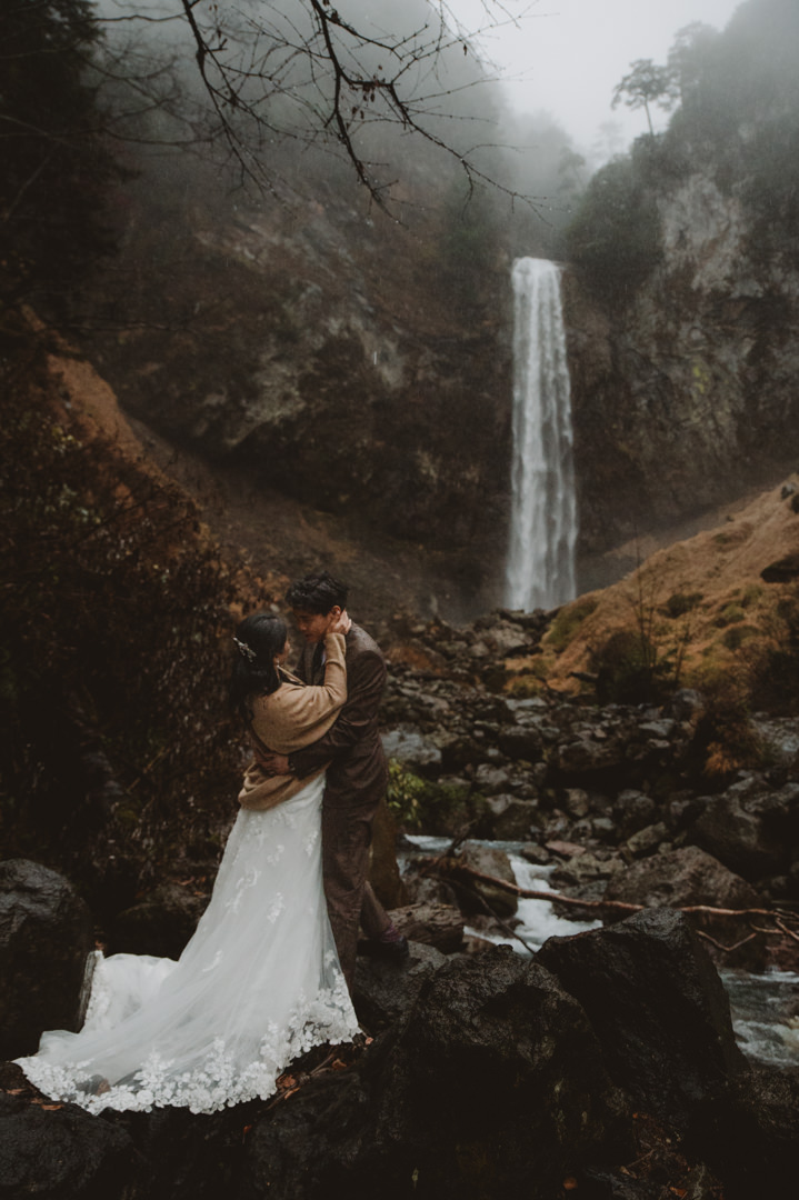 Japan Roadtrip Elopement- Couple is looking at each other in front of the waterfall