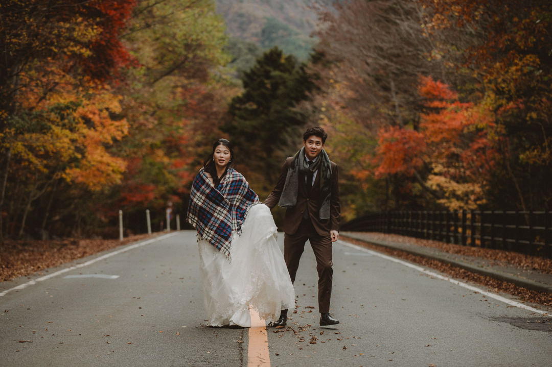 Japan Roadtrip Elopement - Couple is walking on the road surrounded by colorful autumn trees