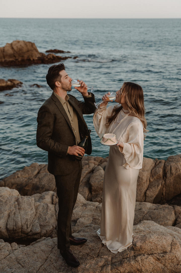 marimurtra elopement - couple celebrating their wedding on the seashore with a cake and champagne