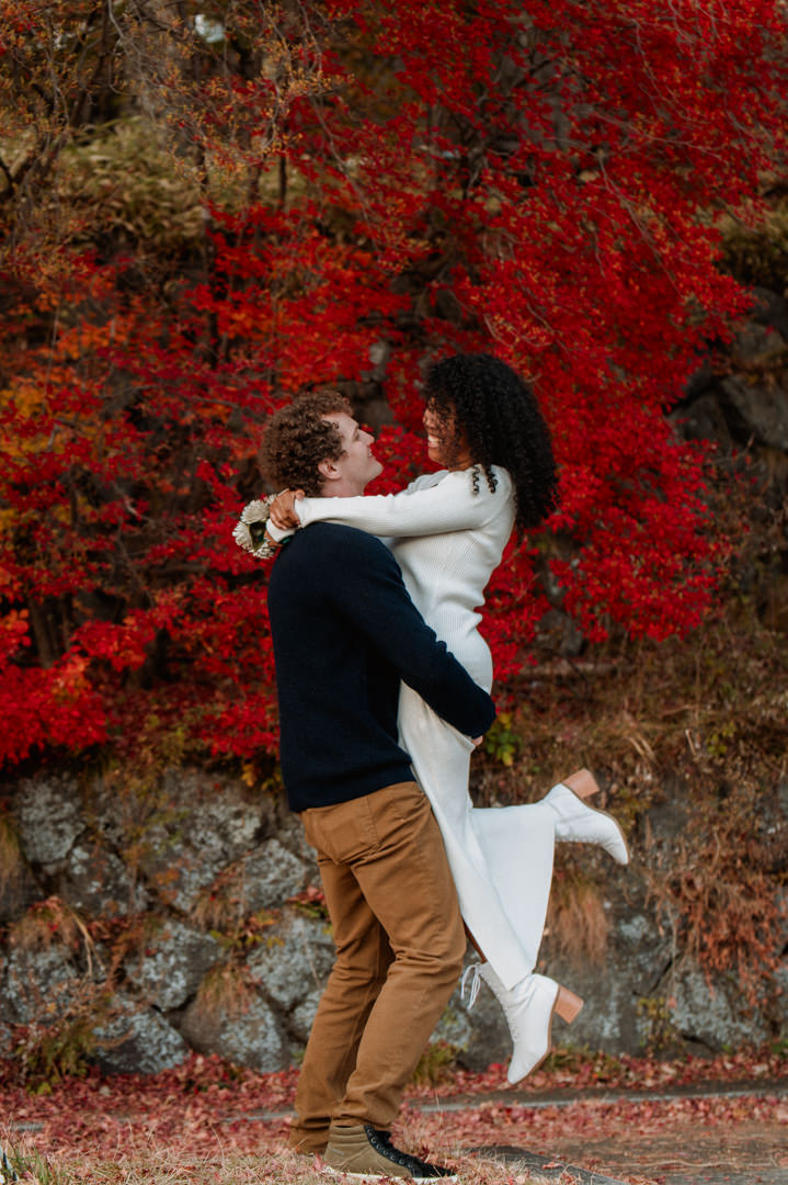 laid-back elopement in japan - groom is picking up bride in front of red leaves 